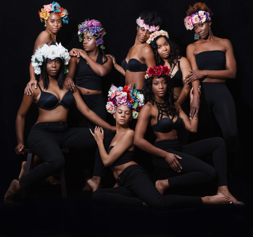 eight African American women of various skin tones dressed in black tops and black pants wearing floral crowns on their heads Captured by a Nashville Portrait Photographer 