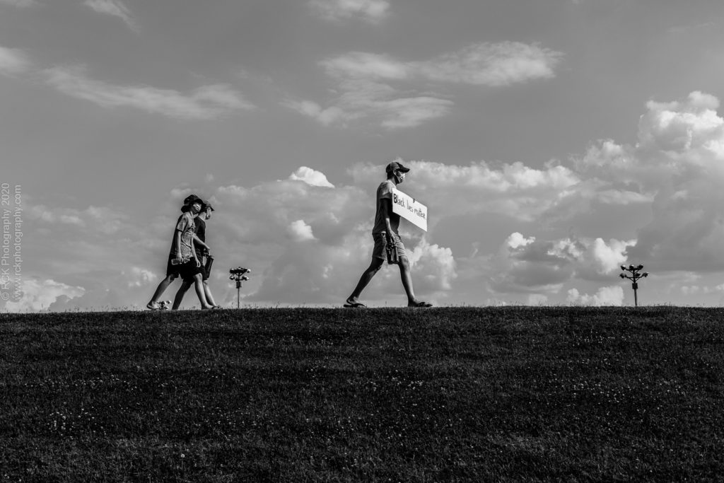 black and white image of a Caucasian Father holding a Black Lives Matter sign  during a protest march with is two teenage sons behind him captured by Denetra Smith of RCK Photography